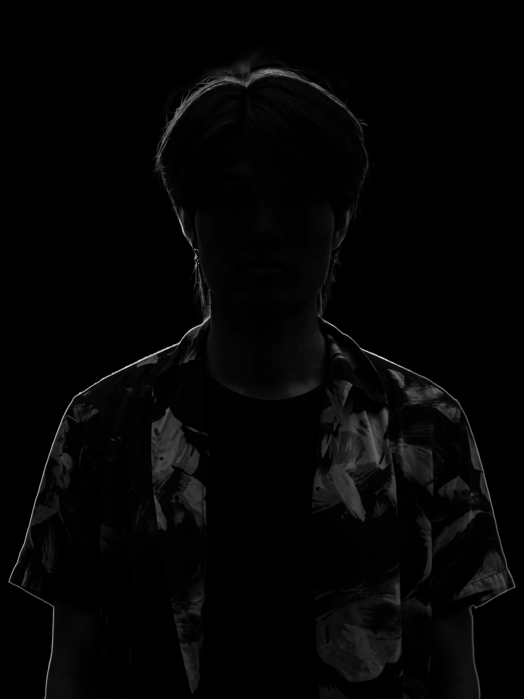 Uefa in silhouette, lit from behind, in an open blue flower-print shirt over a black t-shirt